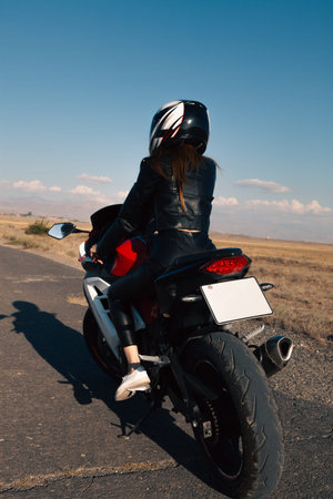Rear view of a young woman sitting on a motorcycle on the road.