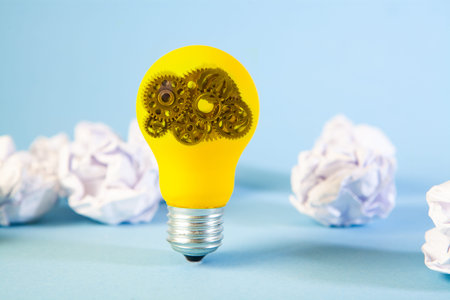 Light bulb with gears inside and crumpled paper balls on blue background