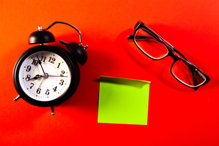 Alarm clock, eyeglasses and sticky note on red background