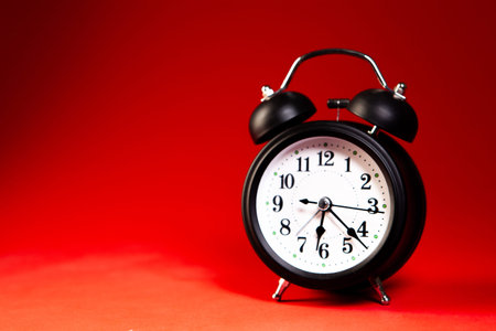Black alarm clock on red background. Time concept. Copy space.
