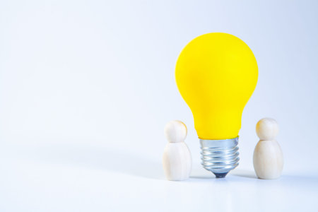 Wooden figures of people and yellow light bulb on a white backgroundの写真素材