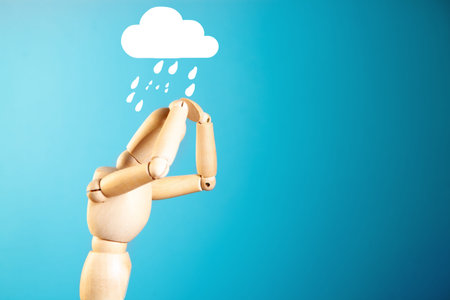 Wooden mannequin holding a cloud with raindrops on blue background