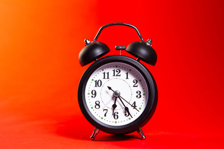 Black alarm clock on a red background. The concept of time.