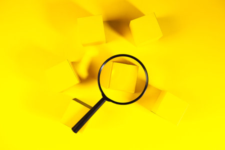 Magnifying glass and yellow cubes on a yellow background. Top view