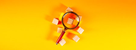 Magnifying glass and wooden cubes on a yellow background. Business concept