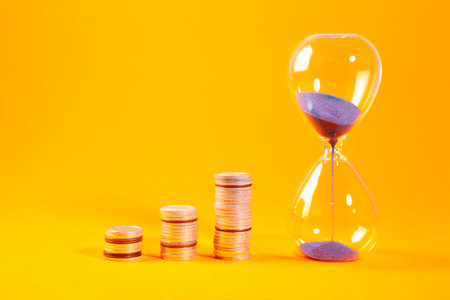 Time is money concept with hourglass and coins on orange background.