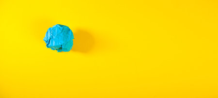 Blue crumpled paper ball on yellow background with copy space.の写真素材