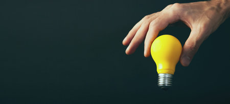 Yellow light bulb in hand on black background. Business idea concept.