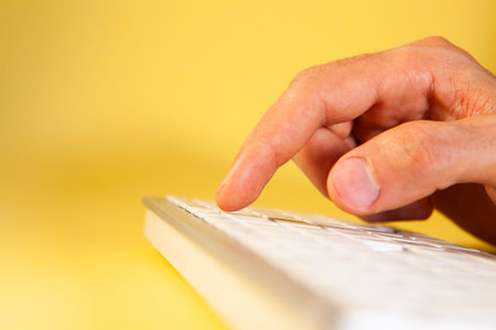 Close up of a male hand typing on a keyboard on yellow background
