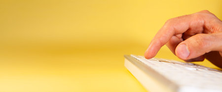 Close up of female hand typing on a keyboard on a yellow background