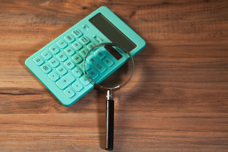 Calculator and magnifying glass on the wooden table, business concept