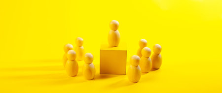 Wooden figures of people stand on a yellow background. The concept of leadership and teamwork.