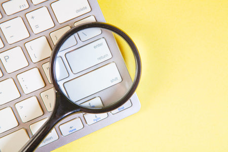 Magnifying glass on a white computer keyboard on a yellow background.
