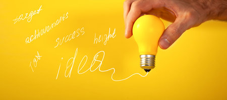 Hand holding a yellow lightbulb on a yellow background with the text