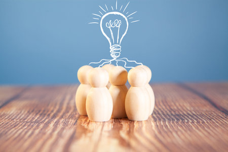 Wooden figures of people and light bulb on a blue background.