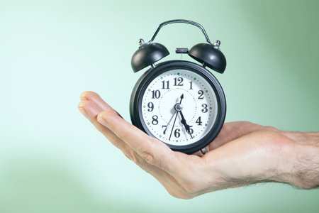 Alarm clock in the hand on a green background. Time concept