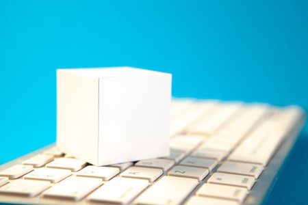 Blank white paper cube on computer keyboard isolated on blue background.