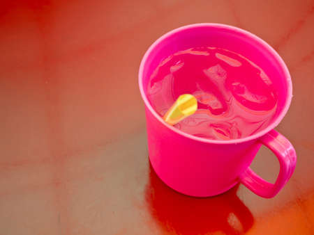 Cool water in pink plastic cup on red tableの写真素材
