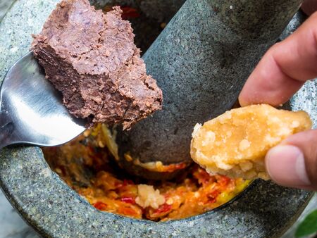 Shrimp paste and sugar put into stone mortar to pound with pepper and garlic