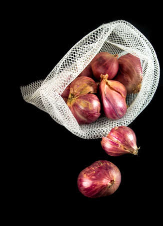 Red onions in mesh bag and some on floor isolated on black backgroundの写真素材