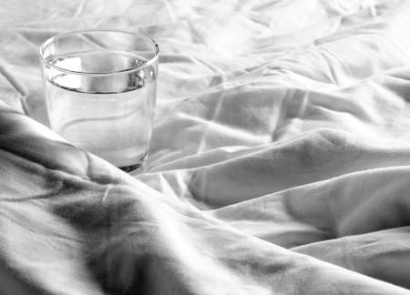 Glass of water on the blanket crumpled on bedの写真素材