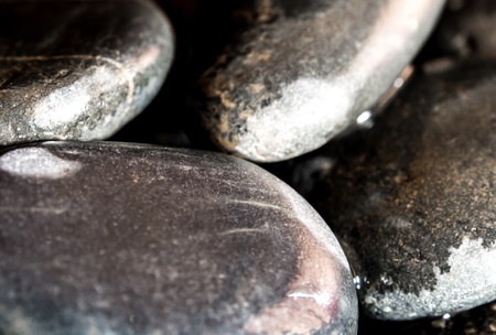 Glossy surface of round black stone on ground beside the waterfallの写真素材