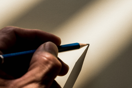 Human's hand holding pencil to write on the paper in shadowの写真素材