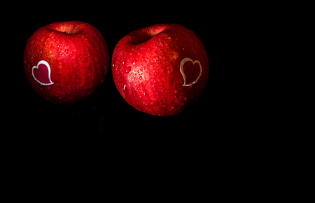 Heart shape sticker and water droplet on glossy surface of freshness red apple on black backgroundの写真素材