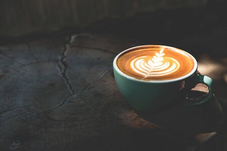 Cup of latte coffee is on top of wood table with shadow and sun light.の写真素材