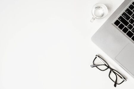 White office desk table with laptop, glass of drinking water and eye glasses. Top view with copy space, flat lay.の写真素材