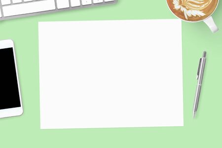 Blank a4 paper is on top of green pastel office desk. Top view, flat lay.の写真素材