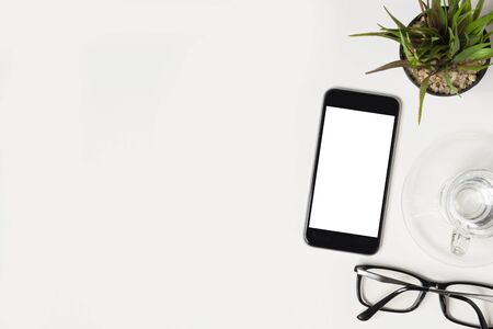 Black smartphone with blank white mockup screen is on top of white office desk table. Top view, flat lay.の写真素材