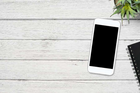 White smartphone with blank screen is on top of wood table. Top view with copy space, flat lay.