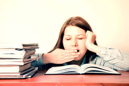 Education conceptual image. Young tired girl yawns during doing her homework.の写真素材