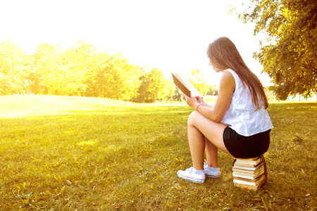 Attractive female college student reading a book and sitting on the stack of books. Education. Back to school conceptual image.の写真素材