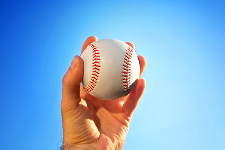 Baseball game. Baseball ball holding by hand against blue clean sky.の写真素材