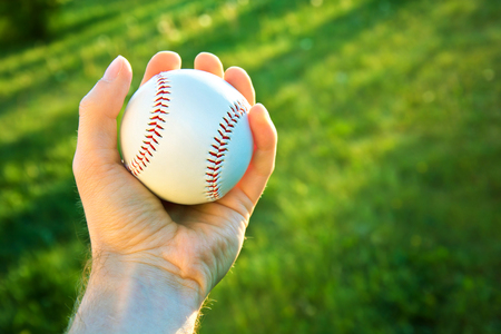Baseball game. Baseball ball holding by hand against green fresh grass.の写真素材
