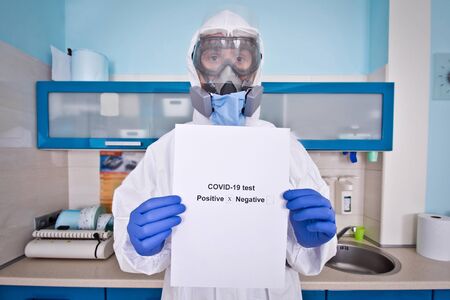 Doctor in protective suit uniform and mask holds coronovirus test results. Coronavirus outbreak. Covid-19 concept.の写真素材