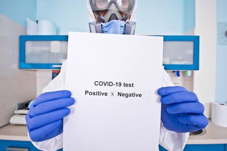 Doctor in protective suit uniform and mask holds coronovirus test results. Coronavirus outbreak. Covid-19 concept.の写真素材