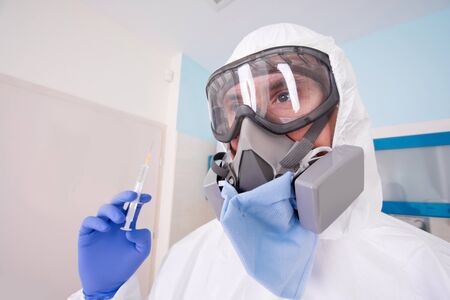 Doctor in protective suit uniform and mask holds injection syringe with vaccine. Coronavirus outbreak. Covid-19 concept.の写真素材