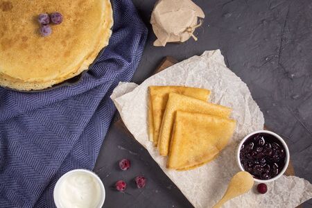 Pancakes for Shrovetide with sour cream and jam, top view. On a wooden Board in the Russian style.