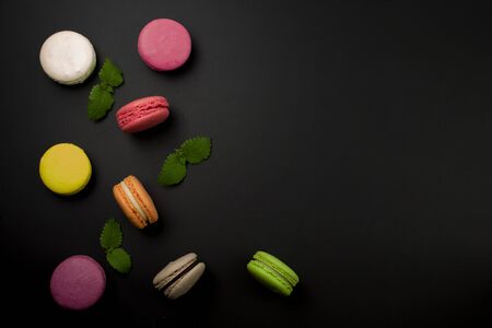 Multicolored macaroons on a black background, top view. Mint leaves next to macaroon.の写真素材