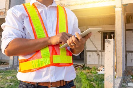 Engineer wears a safety shirt and working with tablet for check Building structure model. Engineering and Architecture concept. Smart working concept.の写真素材