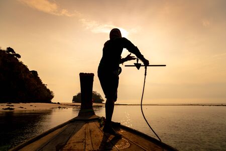 Silhouette of fisherman drops anchor from the boat at krabi, Thailand.の写真素材