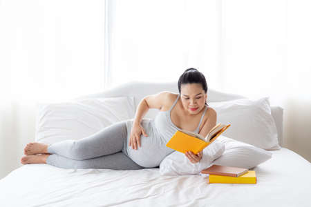 Pregnancy and motherhood concept - Happy pregnant woman reading book on white bed.の写真素材