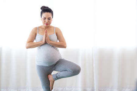 Happy pregnant woman doing yoga at home. Healthy pregnancy, sport, fitness, people and healthy lifestyle concept.の写真素材