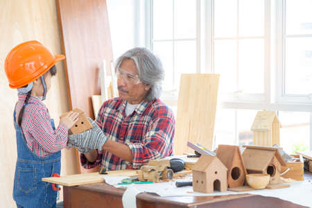 An old carpenter man taught a little girl to make toys from wood. Family, carpentry, woodwork and kid concept.の写真素材