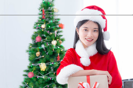 Beautiful woman in santa claus dress with gift box and christmas tree background. Celebrate Christmas and happy New year.の写真素材