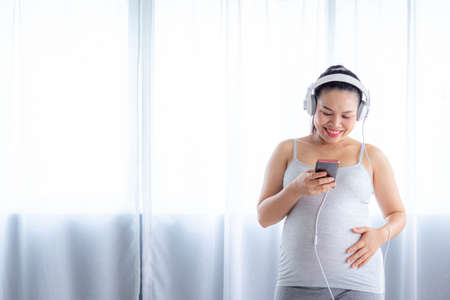 Pregnancy and motherhood concept - Happy pregnant woman listening to music by smartphone and headphones.の写真素材