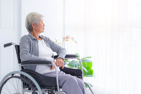 Sad and depressed asian senior woman in a wheelchair at home. Copy space on the window.の写真素材